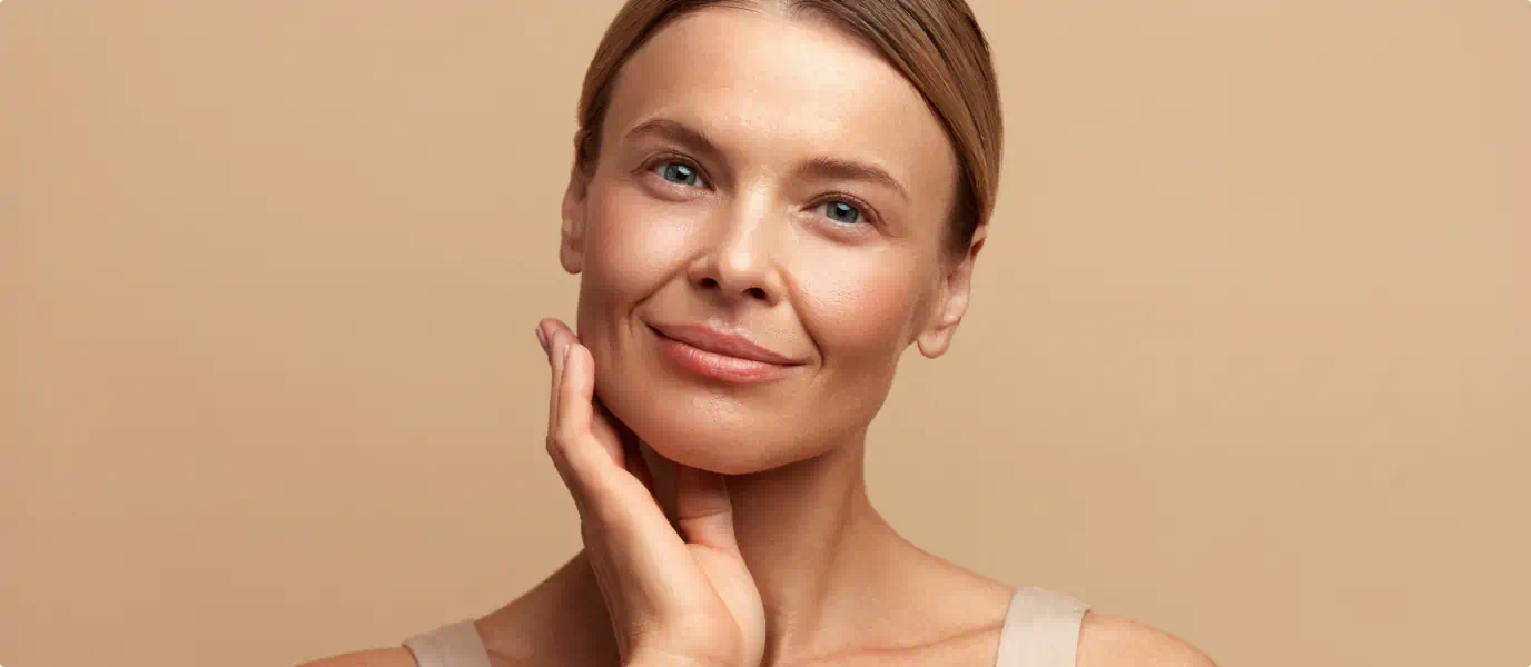 Woman with a radiant complexion touching her face against a beige background