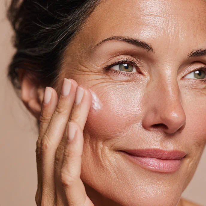 Smiling woman gently applying cream to her cheek