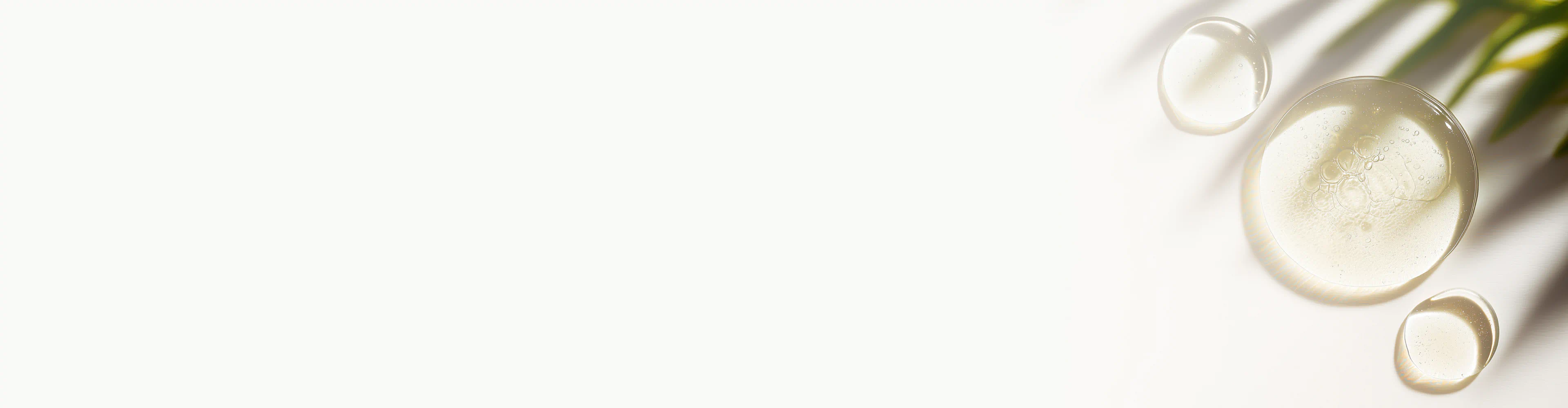 Clear glycerin drops on a white surface with soft shadows