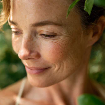 Peaceful woman with dewy skin smiling softly in a lush green setting