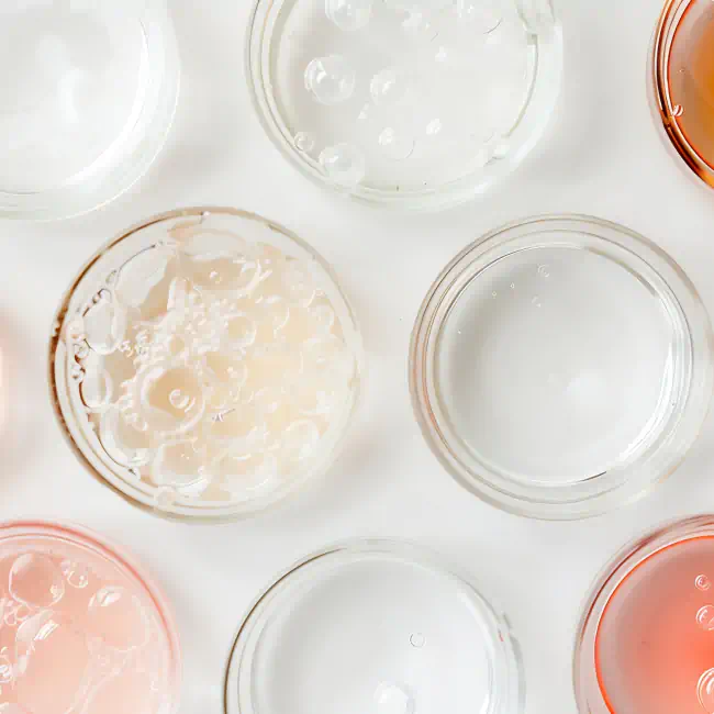 Top view of petri dishes filled with clear, pink, and gel-like skincare solutions