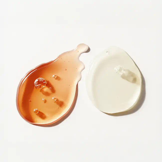 Two glossy skincare serums—one amber, one clear—on a white surface